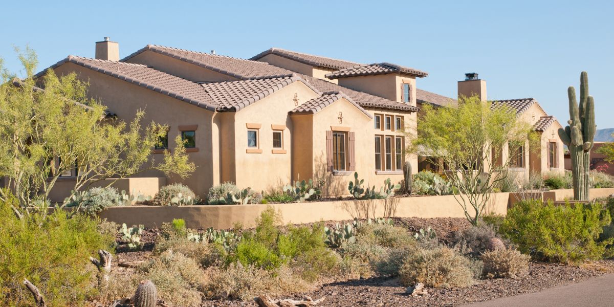 Large desert-style home with beige stucco exterior surrounded by cacti and desert plants.