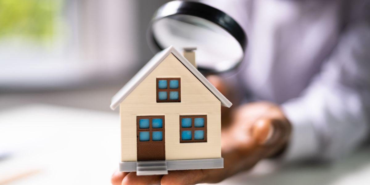 Person holding a small house model while inspecting it with a magnifying glass.