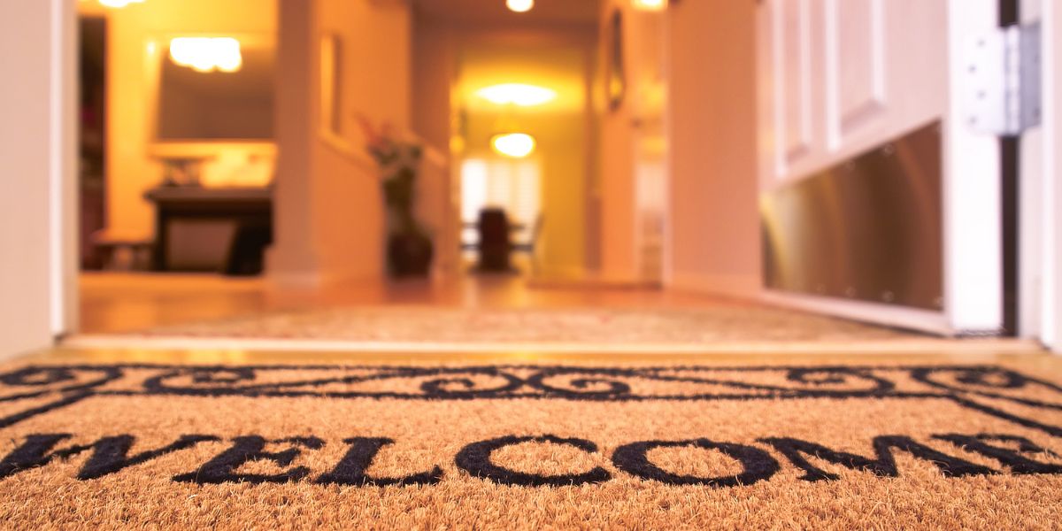 Open front door with a 'Welcome' mat on the floor, leading into a warmly lit home interior.