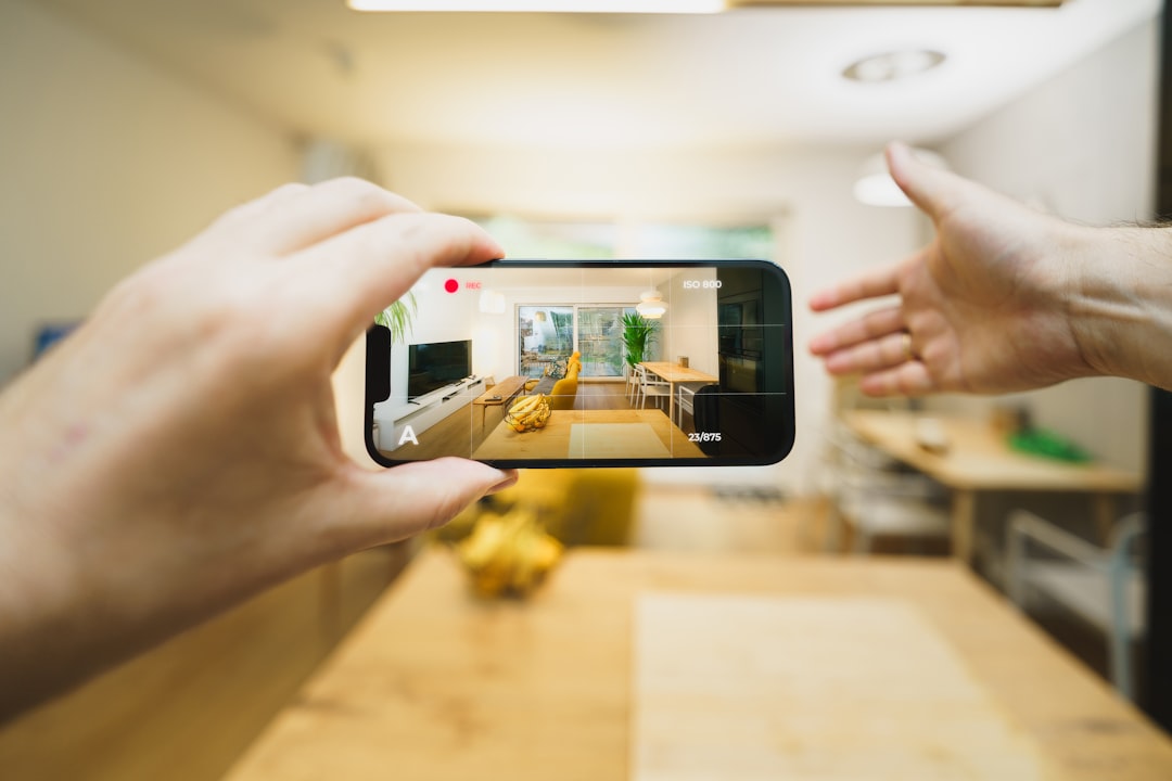 A close-up of a hand holding a smartphone that displays a crisp, professional photo of a modern house, representing real estate in the digital age.