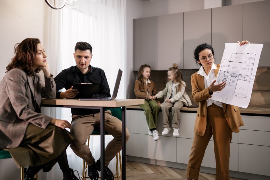 A friendly real estate agent sits with a client at a kitchen island in a modern home, discussing paperwork and illustrating the concept of full-service, professional guidance.
